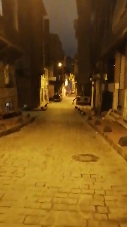 Bir sokak gecesi görünümü, aydınlatmalar hafifçe parlıyor ve taş döşeli zemin dikkat çekiyor.