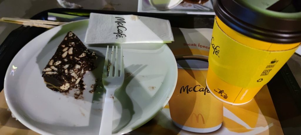 Bir tabakta az kalmış çikolata örtülü bir dilim kek ve yanında McCafé kahve fincanı.