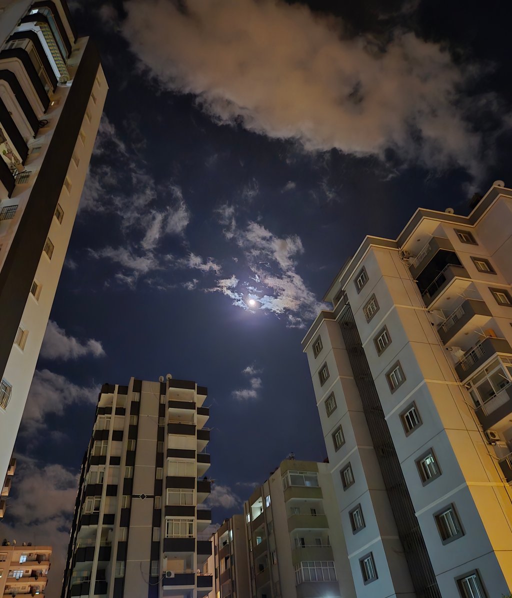 Gece manzarası, binaların arasında dolanan ay ışığı ve bulutlar.