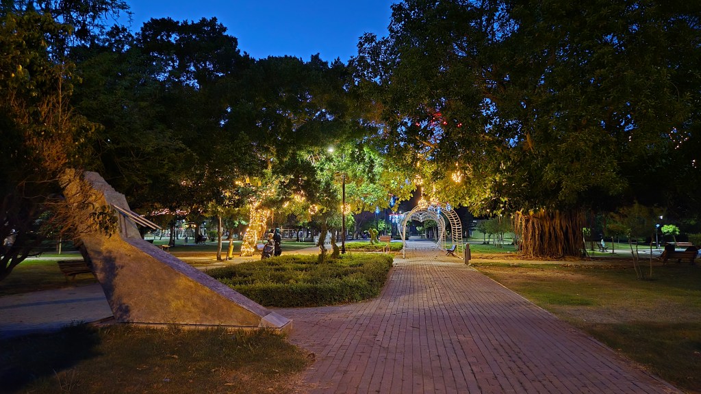 Aydınlatılmış ağaçların ve yolların olduğu bir parkta, akşam saatlerinde çekilmiş gece manzarası.