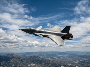 Turkish prototype stealth fighter jet flying above mountains with blue sky and clouds